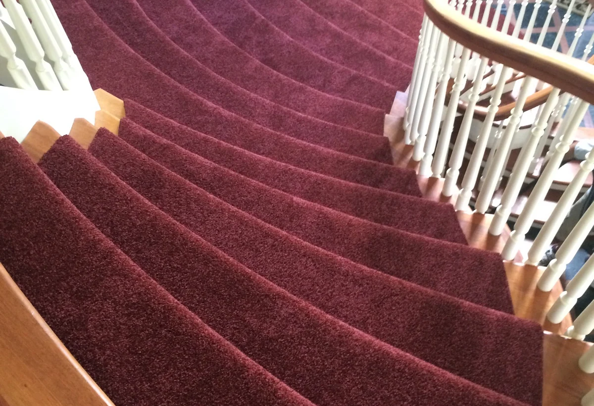 Red curved carpet runner installed on double stairs in Connecticut